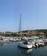 Udsigt over havnen i Fréjus med lystbåde, sejlskibe og byens bygninger under en klar blå himmel.