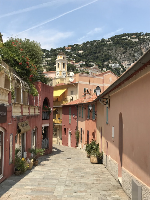 Strada tranquilla con edifici colorati e vista collinare, scattata al Camping Les Lauriers Roses nel sud della Francia.