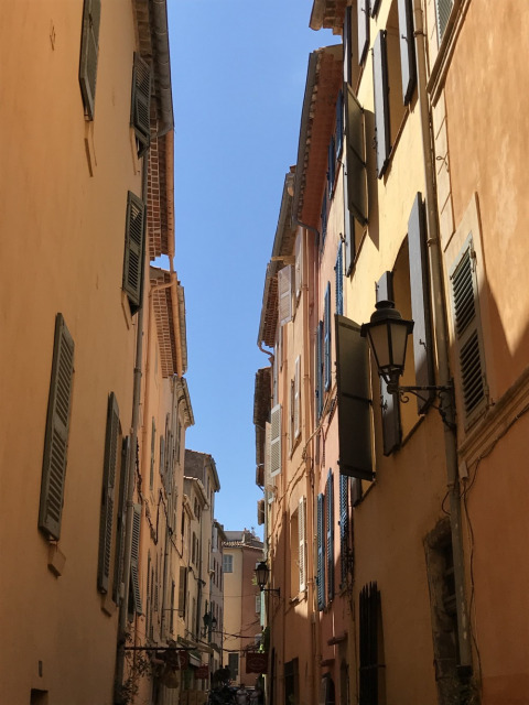 Calle estrecha flanqueada por edificios con contraventanas en Provence-Alpes-Côte d’Azur, Francia.