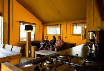 Tre personer sidder sammen i en safari-teltlodge på Camping Roland, Holland, med rustik indretning.