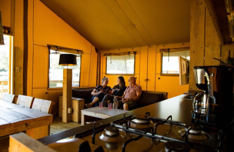 Drie personen zitten samen in een safaritent bij Camping Roland in Nederland met houten inrichting.