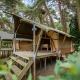 Billede af Duo Lodge teltlodge i en skov med hævet træterrasse, placeret midt i grønne omgivelser.