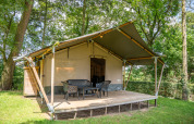 Tenda Safari Lake con veranda in legno e sedie da esterno, immersa tra gli alberi, ideale per il glamping.