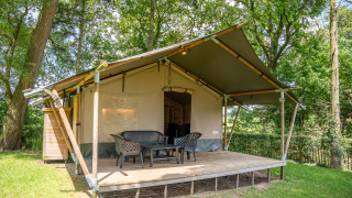Tenda Safari Lake con veranda in legno e sedie da esterno, immersa tra gli alberi, ideale per il glamping.