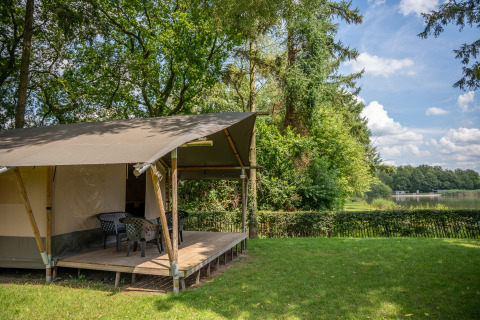 Safaritent aan het meer met veranda en stoelen in groene omgeving bij Familiepark Goolderheide in België.
