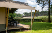 Tienda safari con terraza junto al lago en Familiepark Goolderheide, Bélgica, rodeada de naturaleza.