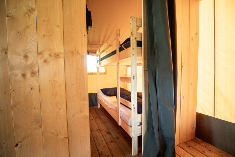 Interieur van een safaritent met stapelbedden, houten vloeren en wanden, verlicht door daglicht.