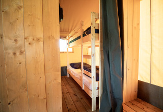 Innenraum eines Safarizeltes mit Etagenbett, Holzböden und Wänden, beleuchtet von Sonnenlicht.