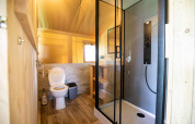 Moderne badkamer in een safaritent met douche, toilet, prullenbak, raam en houten afwerking.
