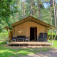 Tenda safari con veranda privata, sedie e tavolo, immersa nel verde della foresta, ideale per glamping.