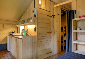 Interno di tenda safari con pareti in legno, piccola cucina e scaffali al Familiepark Goolderheide, Belgio.