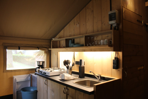 Angolo cucina in una tenda safari con fornello, lavandino e scaffali al Familiepark Goolderheide, Belgio.