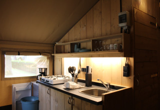 Kitchen area inside a safari tent with stove, sink and shelves at Familiepark Goolderheide in Belgium.