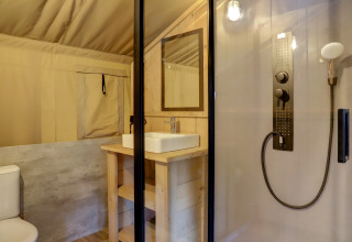 Baño de tienda safari con ducha, inodoro y lavabo en Familiepark Goolderheide, Bélgica.