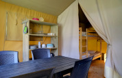 Interior de una tienda safari con mesa de comedor, sillas, estantes y litera en Familiepark Goolderheide, Bélgica.
