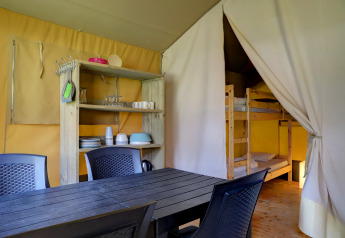 Interior de una tienda safari con mesa de comedor, sillas, estantes y litera en Familiepark Goolderheide, Bélgica.