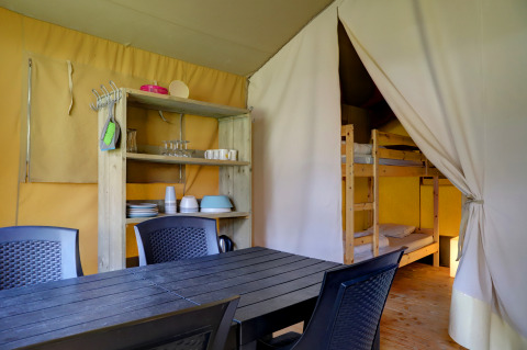 Interno di una tenda safari con tavolo da pranzo, sedie, scaffale e letto a castello al Familiepark Goolderheide, Belgio.