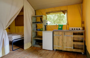 Interior de tienda safari en Familiepark Goolderheide, Bélgica, con cama y una pequeña cocina equipada.