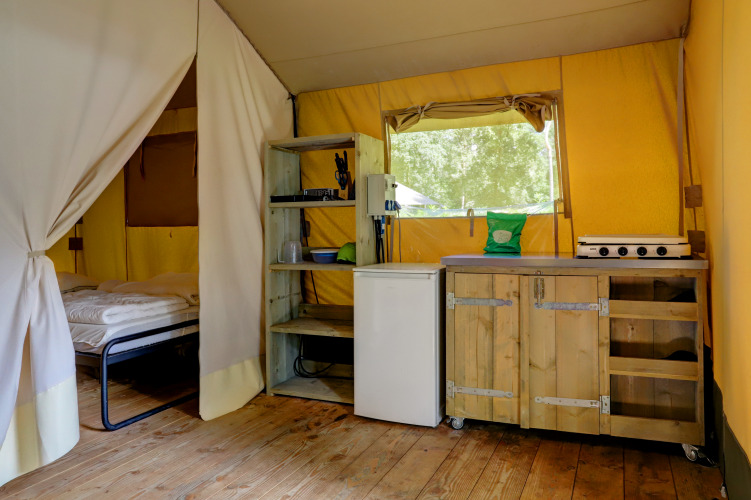 Interior de tienda safari en Familiepark Goolderheide, Bélgica, con cama y una pequeña cocina equipada.