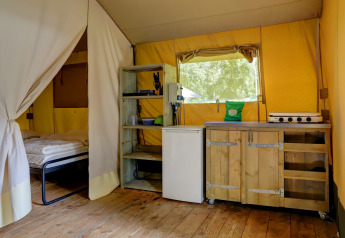 Interior de tienda safari en Familiepark Goolderheide, Bélgica, con cama y una pequeña cocina equipada.