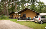 Safaritenten bij Familiepark Goolderheide in België, omringd door bos, terrasmeubels en een geparkeerde auto.