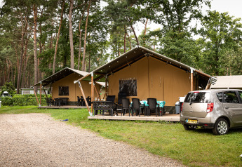 Tiendas safari en Familiepark Goolderheide, Bélgica, entre árboles, con muebles de exterior y un coche aparcado.