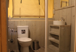 Baño interior en una tienda safari con inodoro, lavabo y espejo en Familiepark Goolderheide, Bélgica.