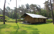 Tienda safari con instalaciones sanitarias y tobogán en Familiepark Goolderheide, Bélgica, rodeada de bosque.
