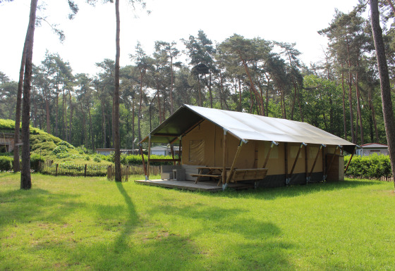 Tienda safari con instalaciones sanitarias y tobogán en Familiepark Goolderheide, Bélgica, rodeada de bosque.