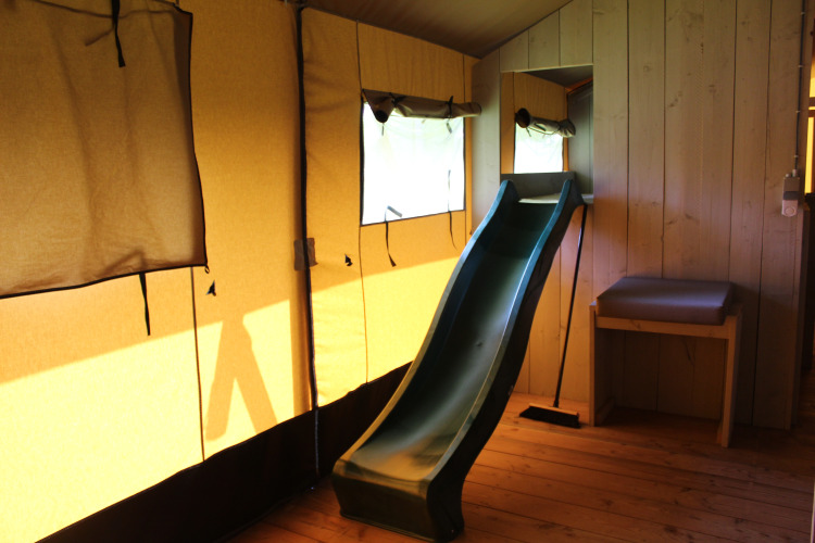 Interior de una tienda safari con tobogán, suelos de madera y luz natural en Familiepark Goolderheide, Bélgica.