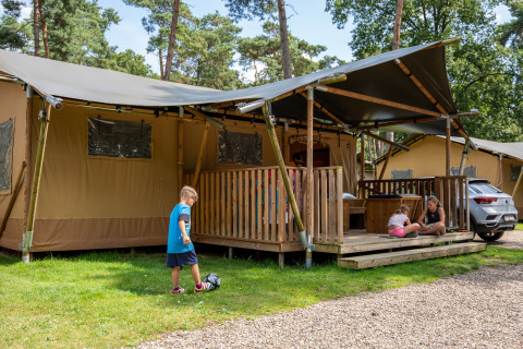 Bambini giocano davanti a una tenda safari con bagno privato al Familiepark Goolderheide, Belgio, tra alberi.