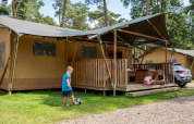 Niños juegan frente a una tienda safari con baño privado en Familiepark Goolderheide, Bélgica, entre árboles.