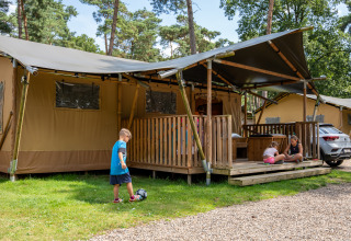 Bambini giocano davanti a una tenda safari con bagno privato al Familiepark Goolderheide, Belgio, tra alberi.