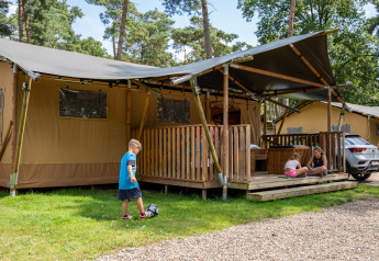 Kinderen spelen aan een safaritent met sanitair op Familiepark Goolderheide, België, omringd door bos.