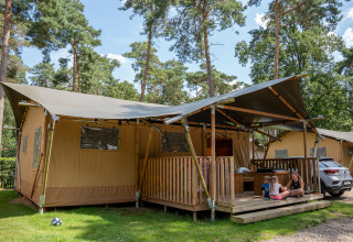 Tienda safari con instalaciones sanitarias en Familiepark Goolderheide, Bélgica, con niños y un adulto fuera.