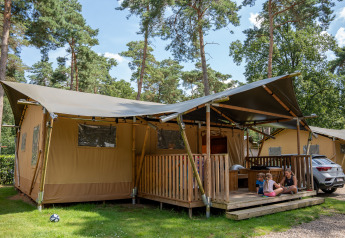 Tienda safari con instalaciones sanitarias en Familiepark Goolderheide, Bélgica, con niños y un adulto fuera.
