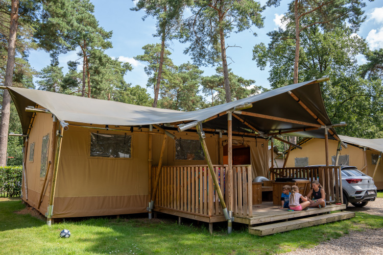 Tienda safari con instalaciones sanitarias en Familiepark Goolderheide, Bélgica, con niños y un adulto fuera.