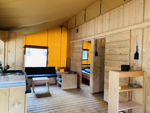 Interior of a safari tent with wooden furniture, kitchenette, seating area, and bedroom at Familiepark Goolderheide, Belgium.