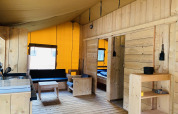 Interno di una tenda safari con mobili in legno, angolo cucina e camera da letto al Familiepark Goolderheide, Belgio.