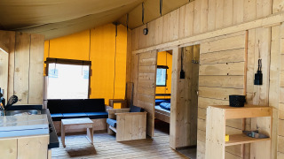 Interior de una tienda safari con muebles de madera, cocina, sala y dormitorio en Familiepark Goolderheide, Bélgica.