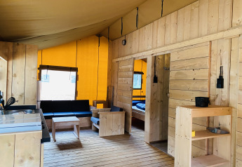 Interno di una tenda safari con mobili in legno, angolo cucina e camera da letto al Familiepark Goolderheide, Belgio.