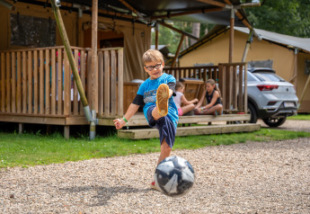 Ragazzo calcia un pallone davanti a una tenda safari con servizi nel Familiepark Goolderheide, Belgio.
