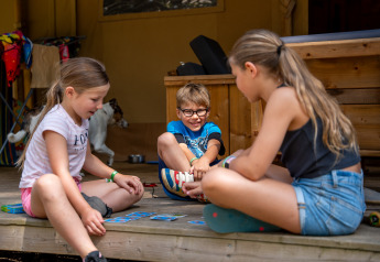 Kinder spielen Kartenspiele auf der Terrasse eines Safarizeltes mit Bad im Familiepark Goolderheide, Belgien.