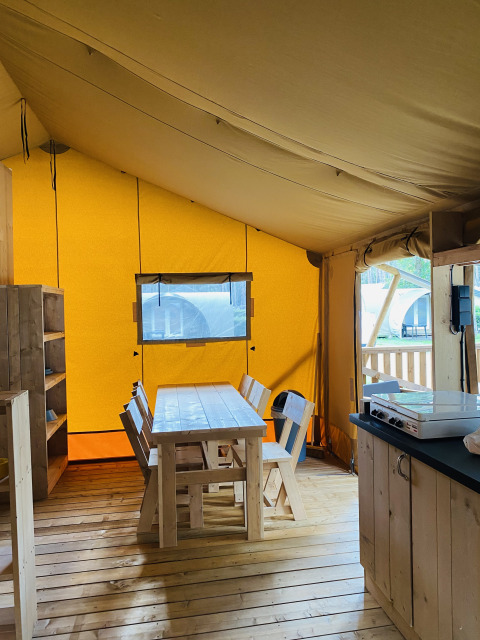 Interior de tienda safari con comedor de madera en Familiepark Goolderheide, Bélgica.