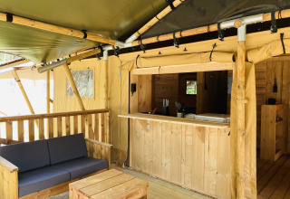 Tienda safari con sanitarios en Familiepark Goolderheide, Bélgica, con sofá y barra de madera.