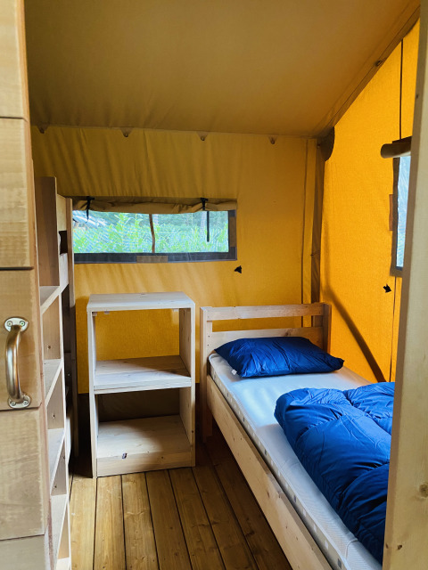 Vista interior de una tienda safari con muebles y cama de madera en Familiepark Goolderheide, Bélgica.