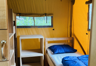 Binnenaanzicht van een safaritent met houten meubels en bed bij Familiepark Goolderheide, België.