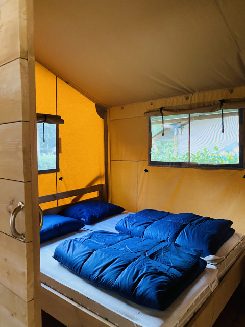 Interno di una tenda safari con letto matrimoniale e biancheria blu al Familiepark Goolderheide, Belgio.