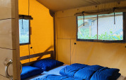 Interieur van een safaritent met tweepersoonsbed en blauwe beddengoed in Familiepark Goolderheide, België.