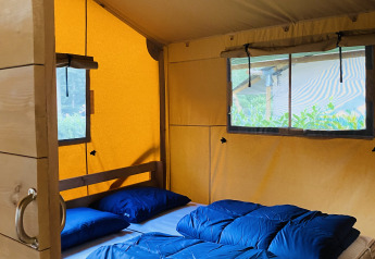 Interno di una tenda safari con letto matrimoniale e biancheria blu al Familiepark Goolderheide, Belgio.